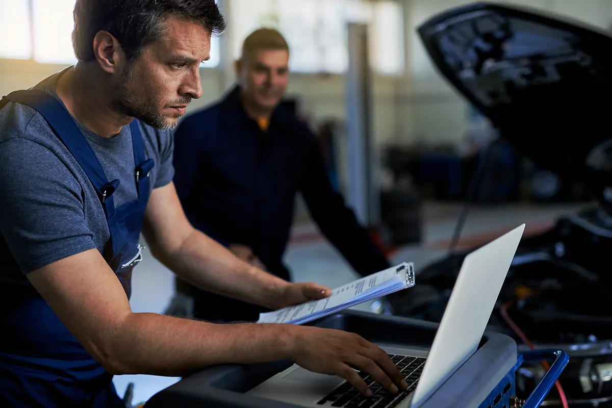 Professional auto technician using dealer-level diagnostic software on a laptop in a modern workshop environment